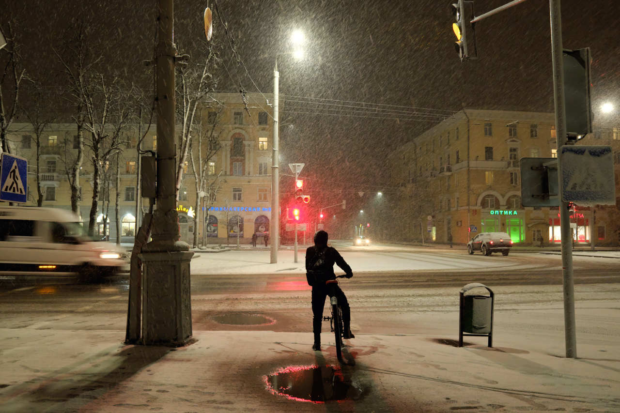 Снег идёт 8 вечер метель перекрёсток велосипедист автомобили прохожие здания светофоры знаки деревья